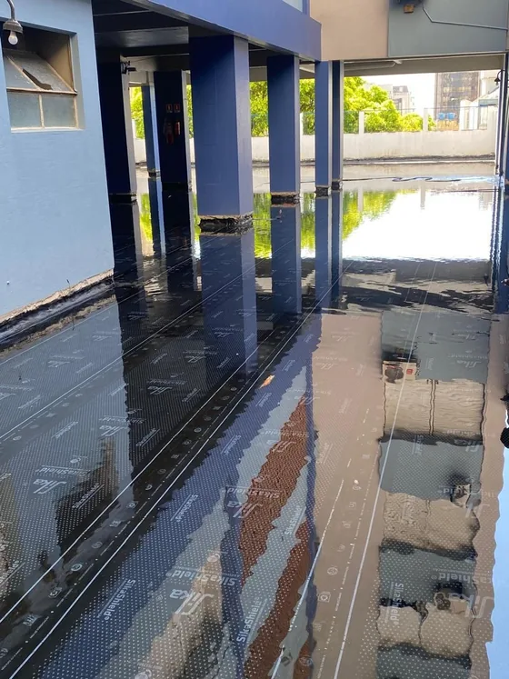 Área sob o pilotis coberta por lâmina d'água sobre a manta asfáltica, com os pilares refletidos