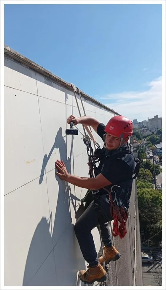 Alpinista bate com martelo em placa de revestimento durante teste de percussão em fachada